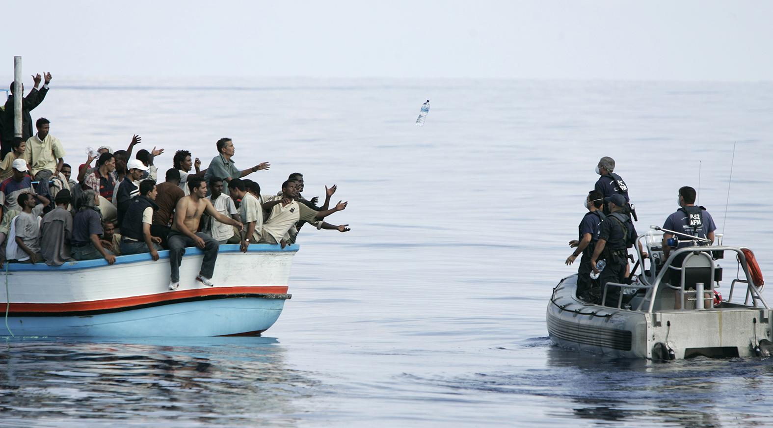 Migrants at sea reach out for water bottles during a rescue.