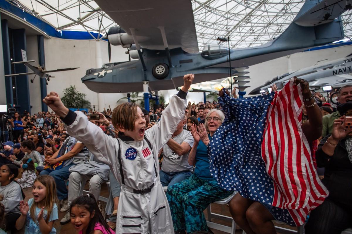 A young boy wearing an astronaut costume cheers next to a woman waving a flag as they watch a live broadcast of the return of the Artemis II crew members to Earth at the San Diego Air and Space Museum. Photo: AFP