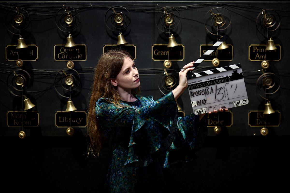 An auction house staff member holds a clapper board backdropped by a bell wall, both used in the TV and film series &lsquo;Downton Abbey&rsquo;.