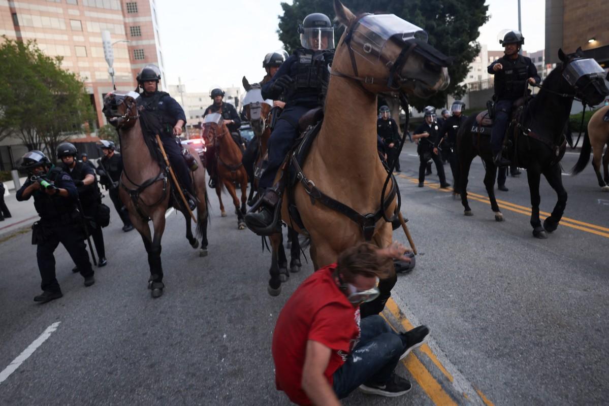 A protester is knocked to the ground by an LAPD mounted police horse as officers evacuate the area. Photo: AFP