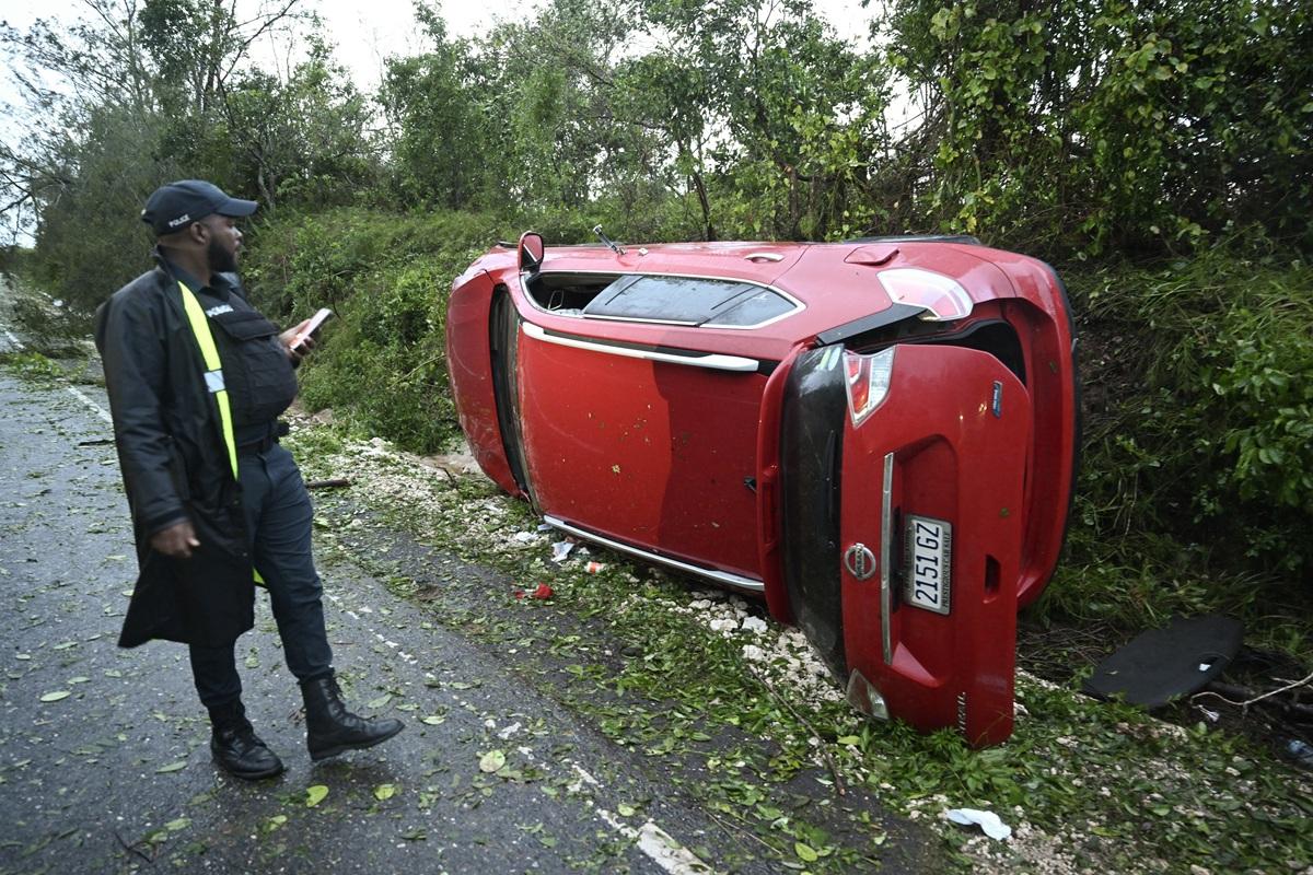 A police officer inspects a car damaged by a fallen tree after the passage of Hurricane Melissa in Manchester, Jamaica. AFP
