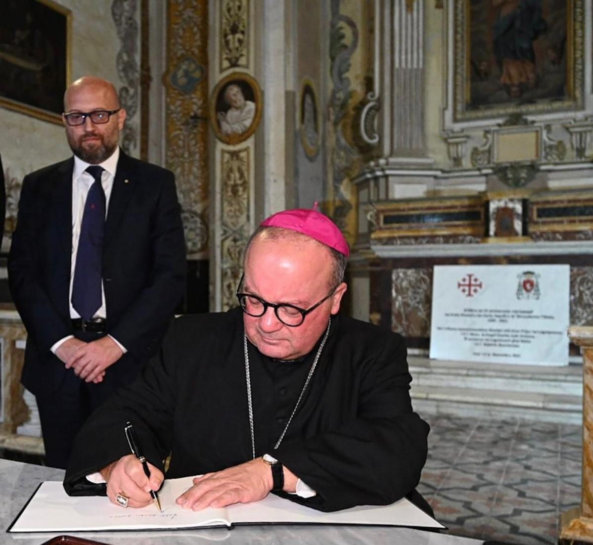 Archbishop Charles Scicluna signing the commemorative book on the occasion of the 25th anniversary of the presence in Malta of the Equestrian Order of the Holy Sepulchre of Jerusalem. Looking on is Ambassador Roberto Buontempo, Lieutenant of the Order.