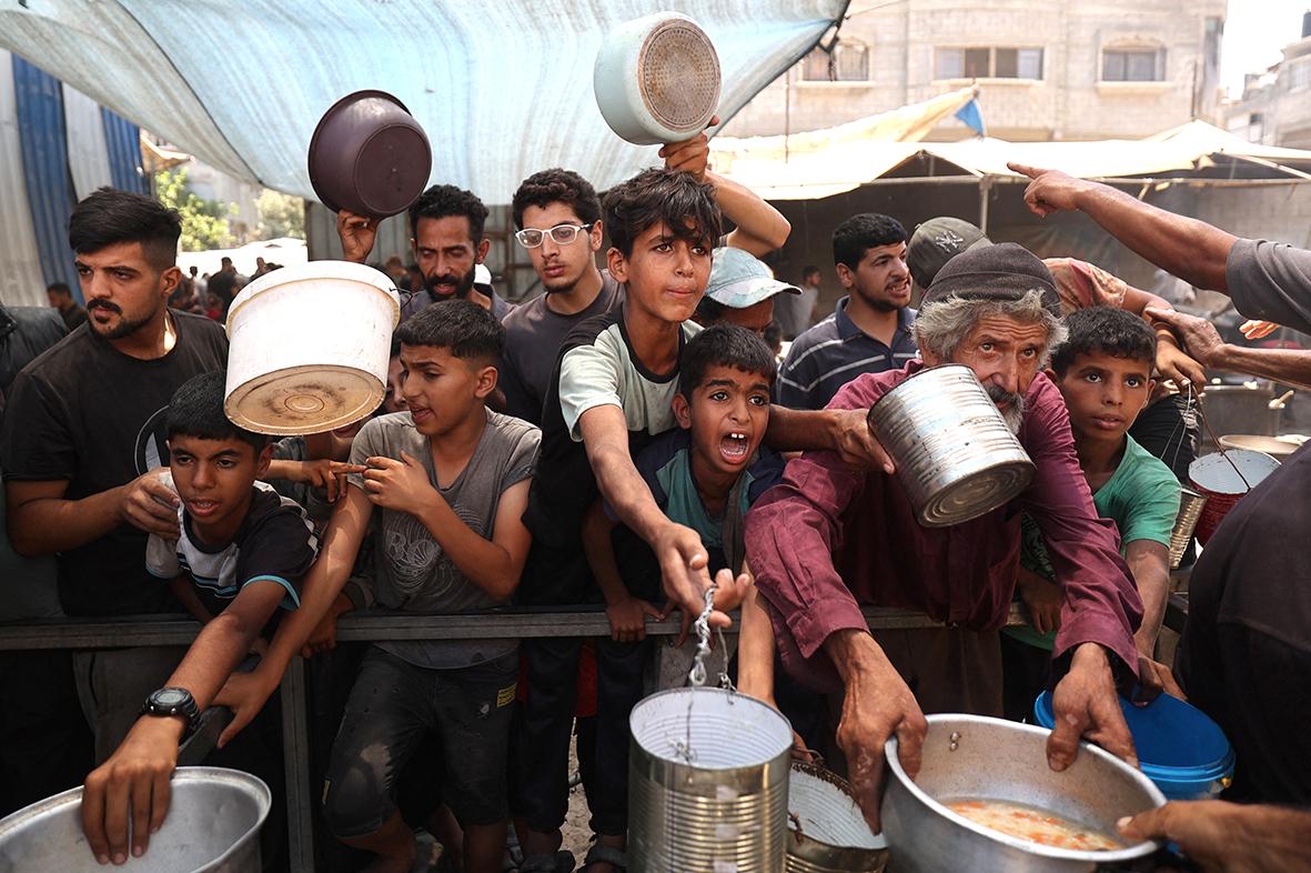 Palestinian children queue for a portion of hot food distributed by a charity kitchen at the Nuseirat refugee camp in the central Gaza Strip. Photo: Eyad Baba / AFP