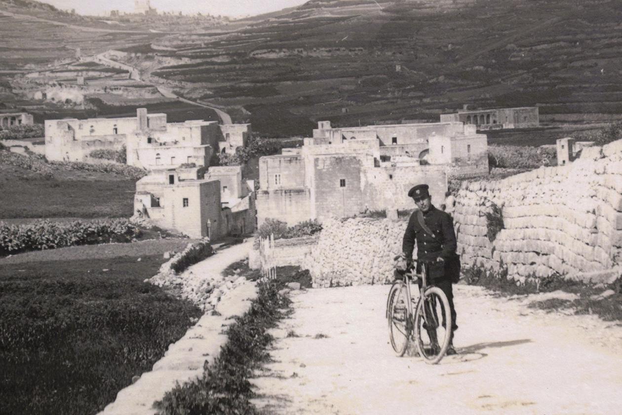 A postcard by Mikiel Farrugia of a policeman on a bicycle on Żebbuġ Road, Gozo.