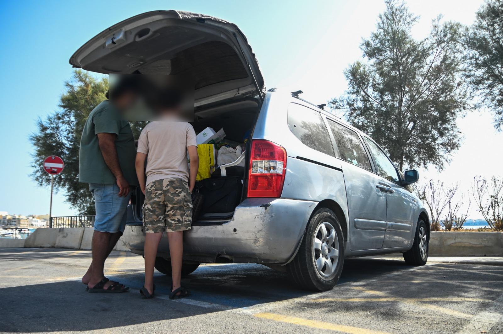 Father and son look into the boot of the van - their home - where they keep all their belongings including medication for a sick child. Photo: Jonathan Borg