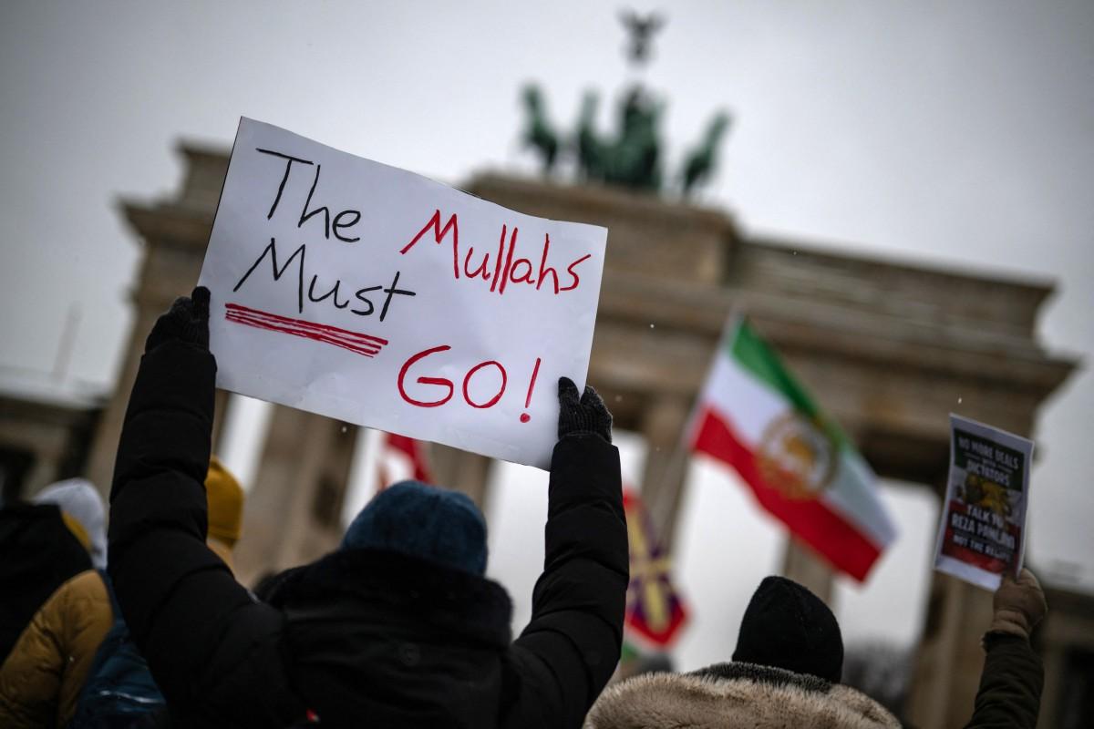 A protester holds a placard reading 'The Mullahs must go!' as flags are waved in front of the Brandeburg Gate during a rally in Berlin, Germany on Monday. Photo: AFP