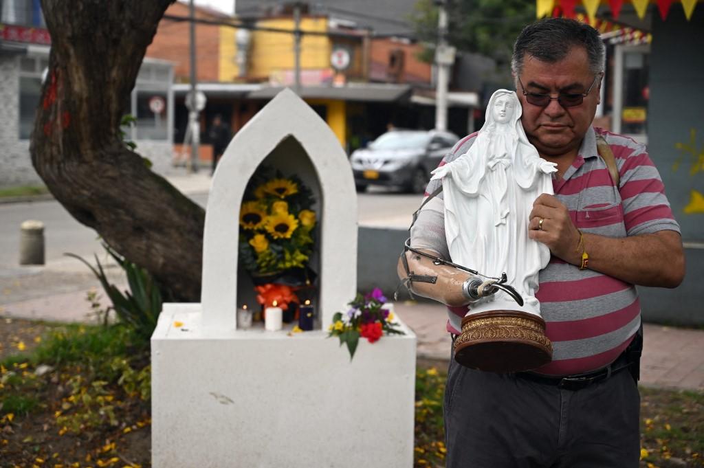 A man holds a religious figure with his prosthetic arm while paying tribute to Colombian presidential candidate Miguel Uribe at the site where he was shot. Photo: AFP