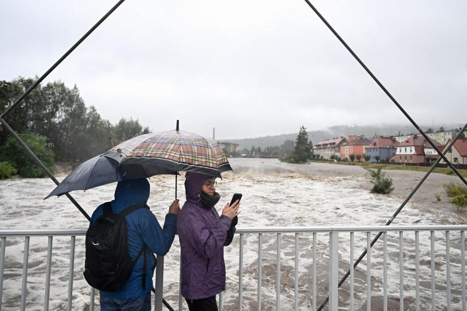 People shelter from the rain under umbrellas as they walk across a bridge over the Biala River in Glucholazy, southern Poland, AFP file photo.