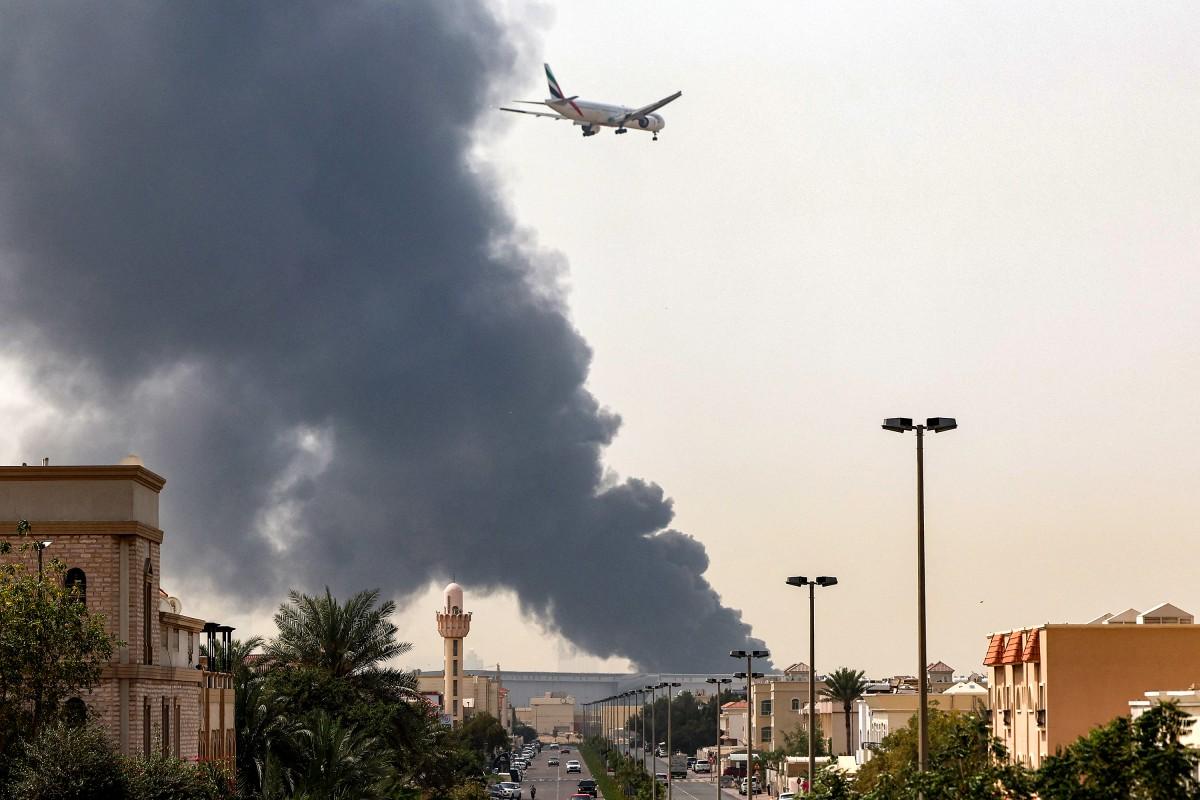 An Emirates aircraft prepares for landing as a smoke plume rises from an ongoing fire near Dubai International Airport in Dubai on Monday. Photo: AFP