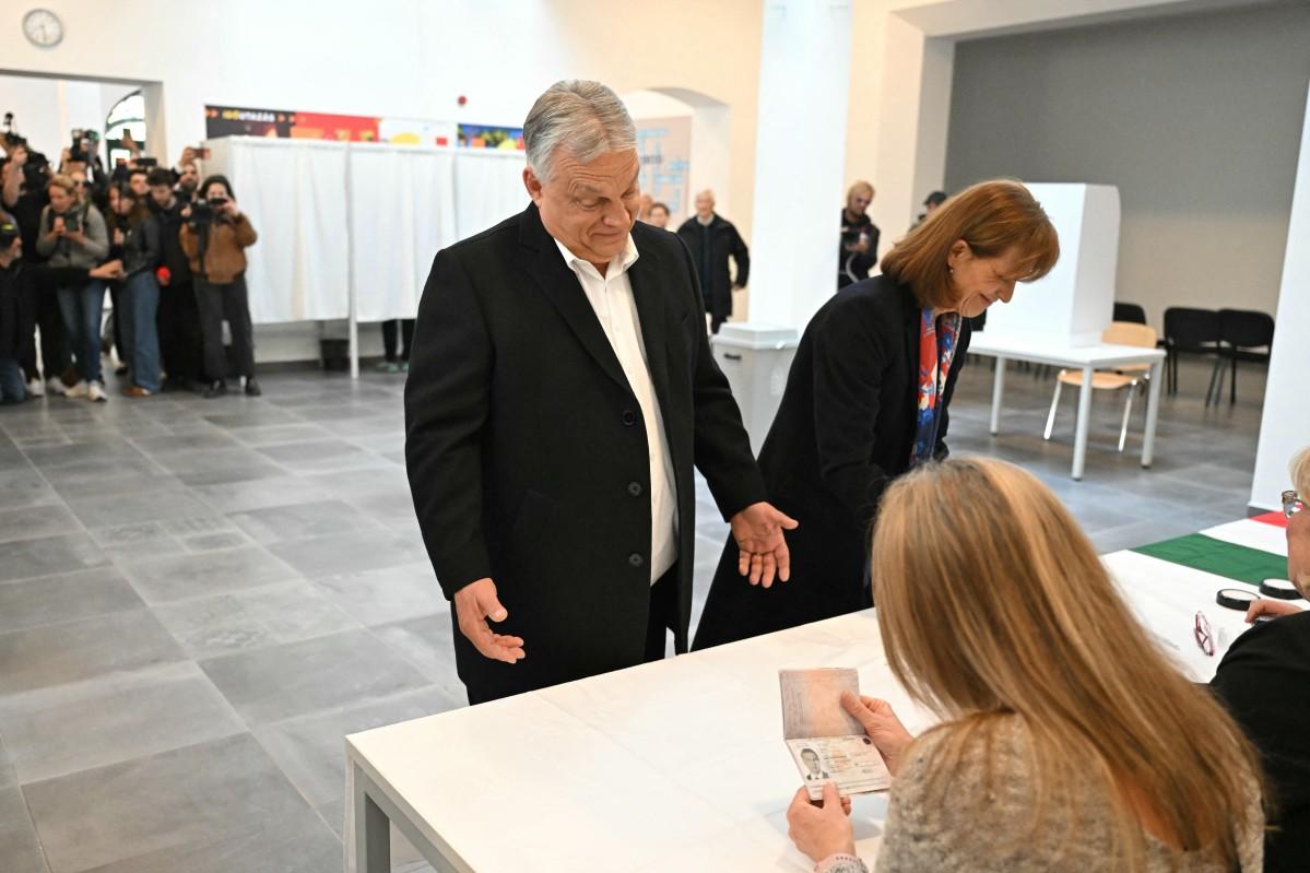 Hungarian Prime Minister Viktor Orban (L) presents his passport beside his wife at a polling station. Photo: ATTILA KISBENEDEK / AFP.
